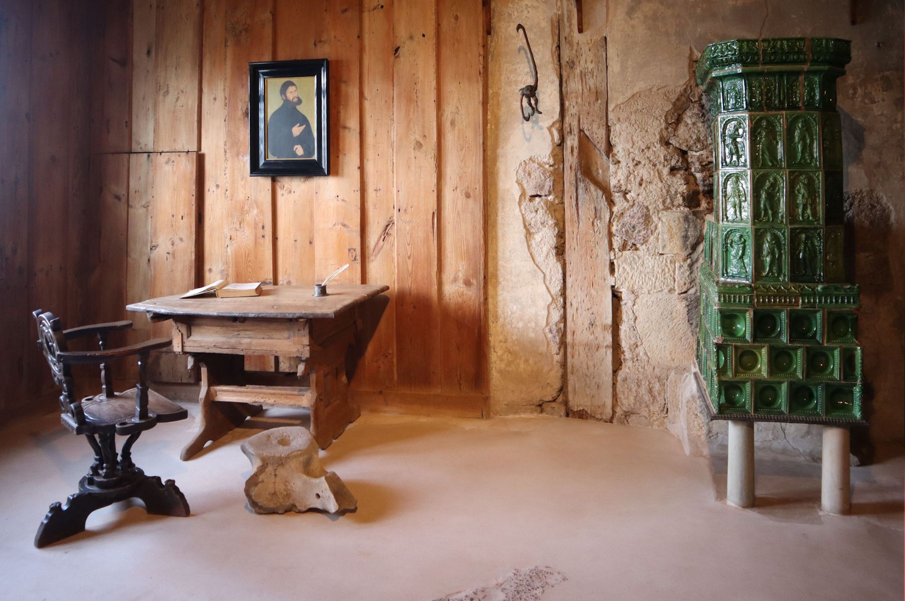 Luthers Stube in der Wartburg bei Eisenach. Die Einrichtung ist nicht original. Der legendäre Tintenklecks - weil Luther ein Tintenfass nach dem ihn versuchenden Teufel geworfen habe - wird nicht mehr restauriert, da er unhistorische ist; er war links neben dem Kachelofen.