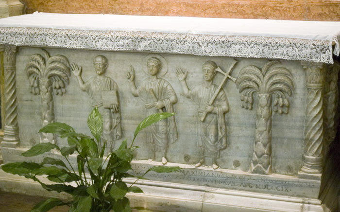Sarkophag mit den Gebeinen von Maximianus und Bischof Exuperantius, 415, in der Kathedrale in Ravenna. Im Relief dargestellt ist Christus (Mitte) mit Paulus (links) und Petrus (rechts).