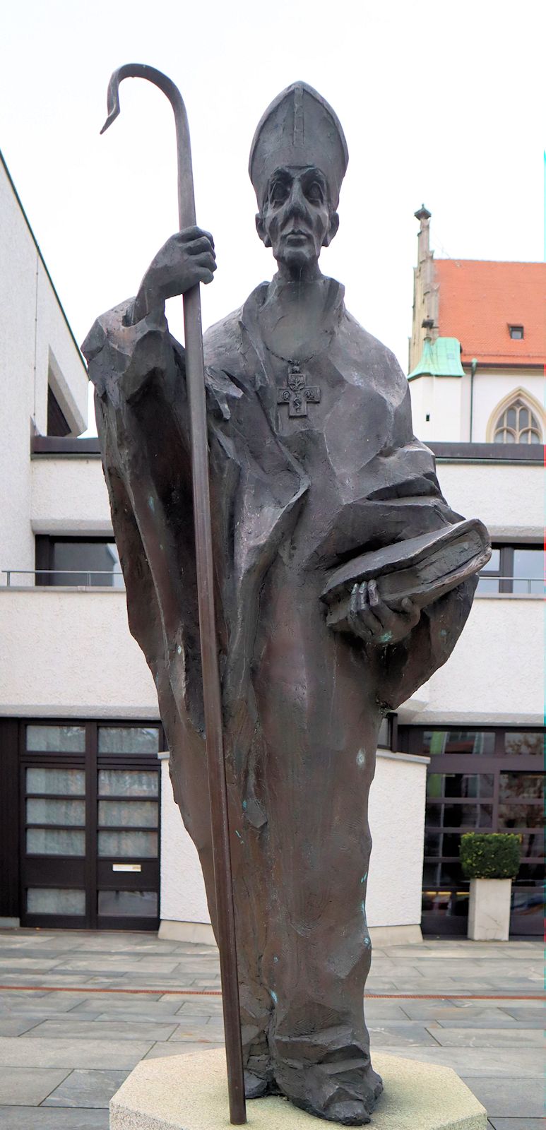 Klaus Backmund: Statue, 1993, vor dem Tagungshotel Haus Sankt Ulrich, erbaut an der Stelle des früheren Benediktinerklosters an St. Ulrich und Afra in Augsburg; sie wurde 2024 auch zum Motiv einer Briefmarke der deutschen Post